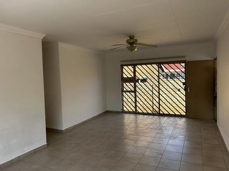 A spacious, empty living room featuring neutral tiled flooring, a ceiling fan, and a large sliding door with a security gate leading outdoors.