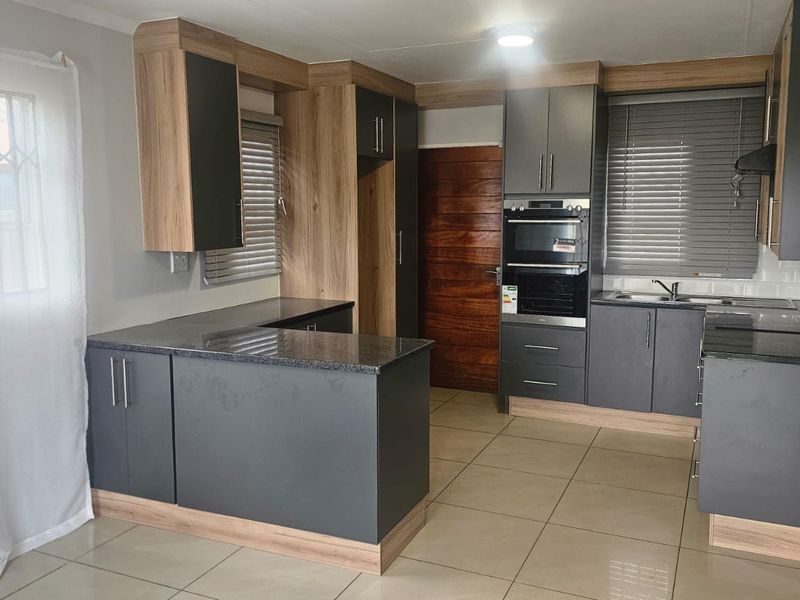 Modern kitchen featuring dark grey and wood-tone cabinetry, granite countertops, built-in oven, extractor fan, and tiled flooring in a clean, functional layout.
