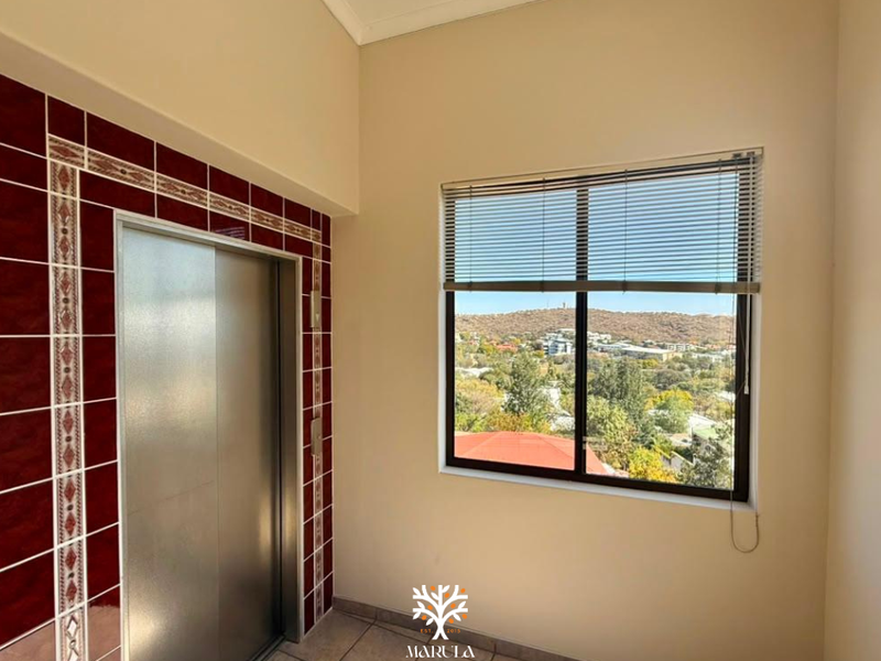 A bright hallway featuring a private elevator with decorative tile surround and a large window offering scenic hillside views.