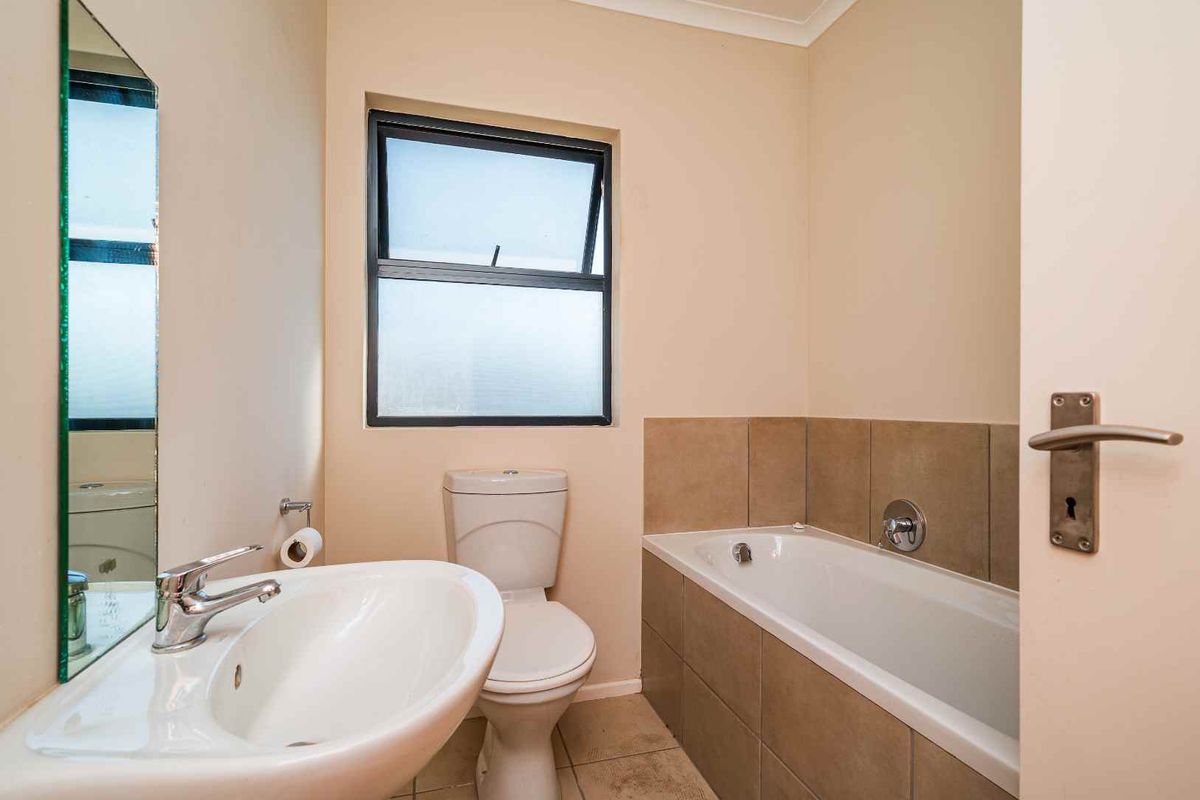 A functional bathroom featuring a pedestal basin, toilet, and a tiled bathtub with neutral wall finishes and a frosted window for privacy.
