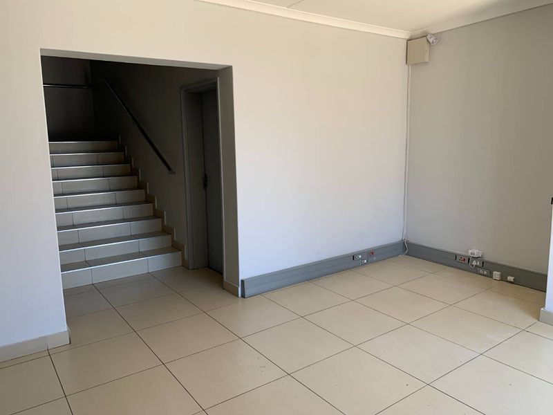 An empty industrial hallway featuring tiled flooring, a staircase, and integrated electrical trunking along the baseboards.