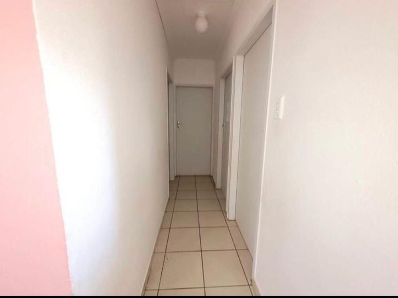 A simple, neutral hallway featuring tiled flooring and white walls, providing access to multiple rooms within the property.