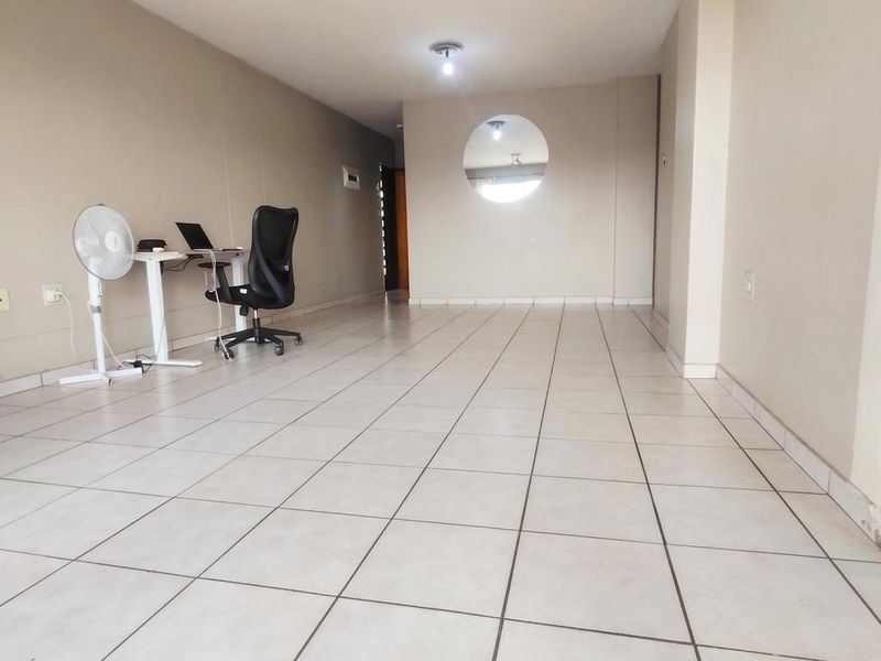 A spacious, open-plan living area featuring neutral wall tones and ceramic floor tiles, highlighted by a unique circular architectural cutout.