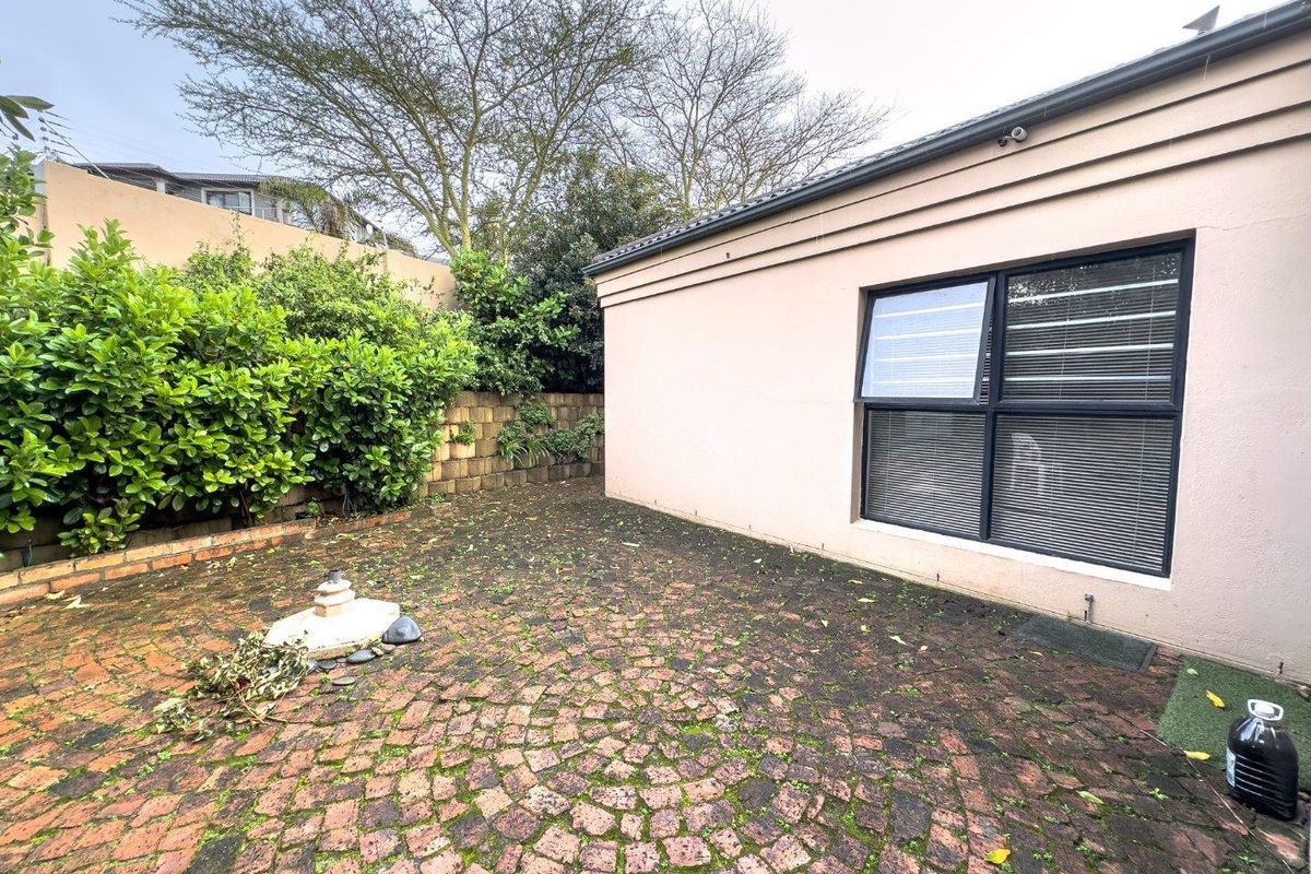 A rear exterior patio area featuring brick paving, a retaining wall, and aluminum window frames, requiring maintenance to address surface growth and weathering.