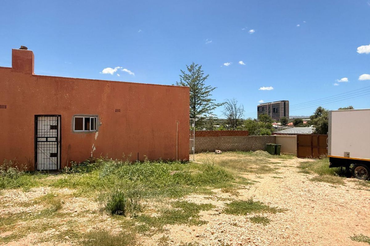 Rear exterior view of the property showing a large unpaved yard, masonry boundary wall, and the rear facade with visible plaster and paint deterioration.