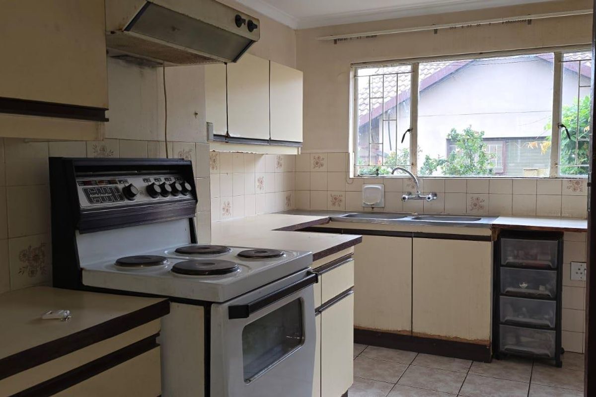 A dated kitchen featuring original cabinetry, a freestanding stove with extractor fan, and a double basin sink with tiled splashbacks.