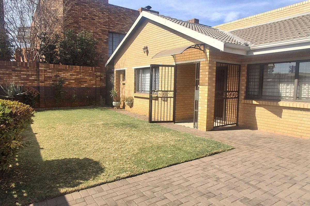 Rear view of the property featuring a face brick facade, paved patio area, and a well-maintained lawn with secure gated access.