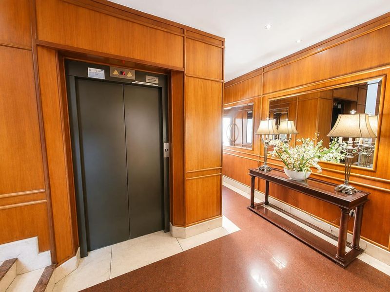Elegant penthouse hallway featuring rich wood paneling, stone flooring, and a private elevator access point with integrated mirror detailing.
