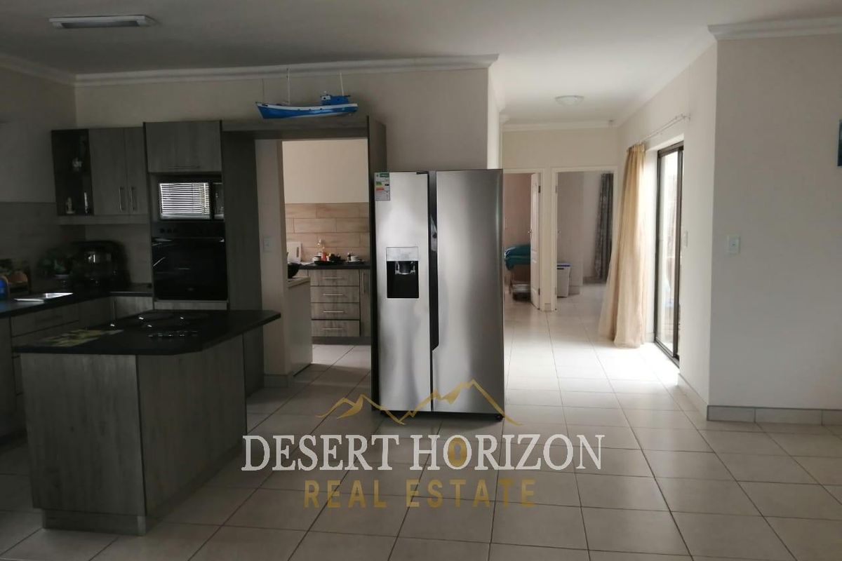 Open plan kitchen and living area featuring modern grey cabinetry, a central island, tiled flooring, and direct access to an outdoor space.