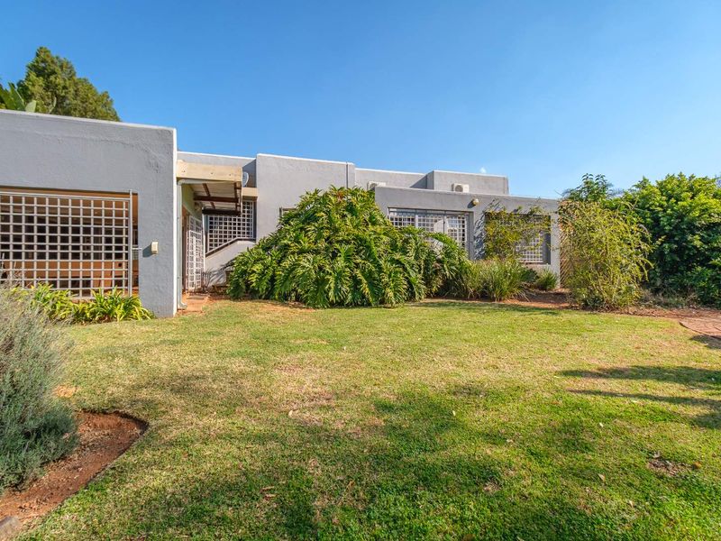 Rear view of the property featuring a lawn, established garden, and security gates on the building facade.
