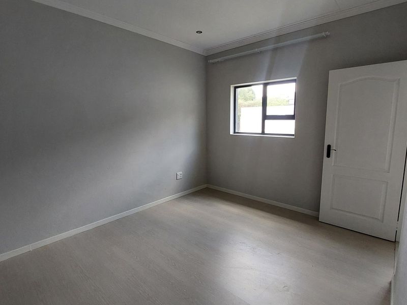 A clean, empty bedroom featuring neutral grey walls, light-toned laminate flooring, and a modern aluminium window frame.