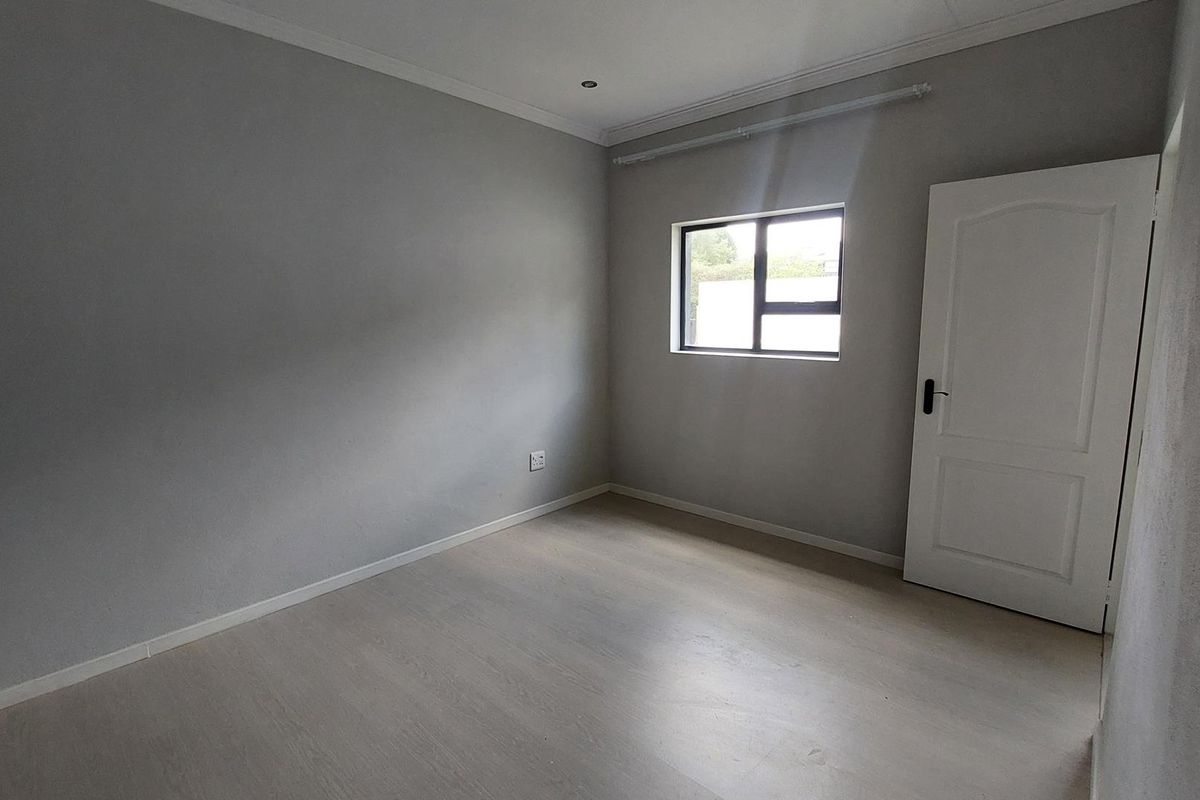 A clean, empty bedroom featuring neutral grey walls, light-toned laminate flooring, and a modern aluminium window frame.