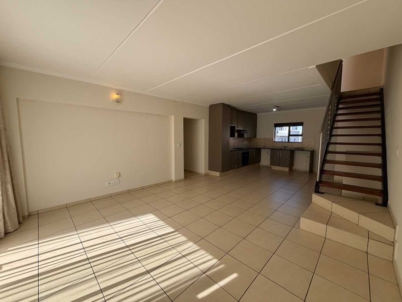 Spacious open-plan living area featuring tiled flooring, a functional kitchen with built-in cabinetry, and an internal staircase leading to the upper level.