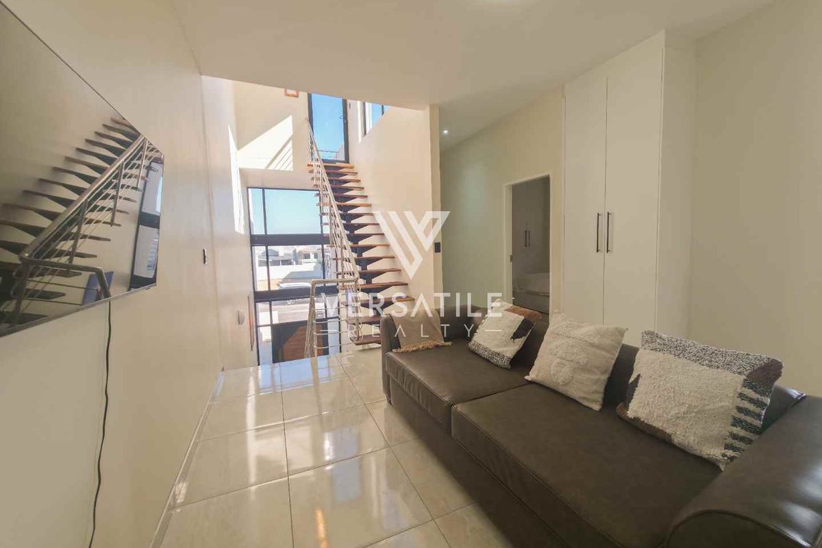 Modern living area featuring tiled flooring, built-in storage cupboards, and an open staircase leading to the upper level.