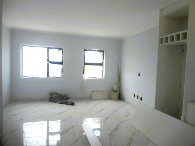An empty living room featuring polished marble-look floor tiles, built-in shelving, and aluminium-framed windows, currently in a state of final construction finishing.