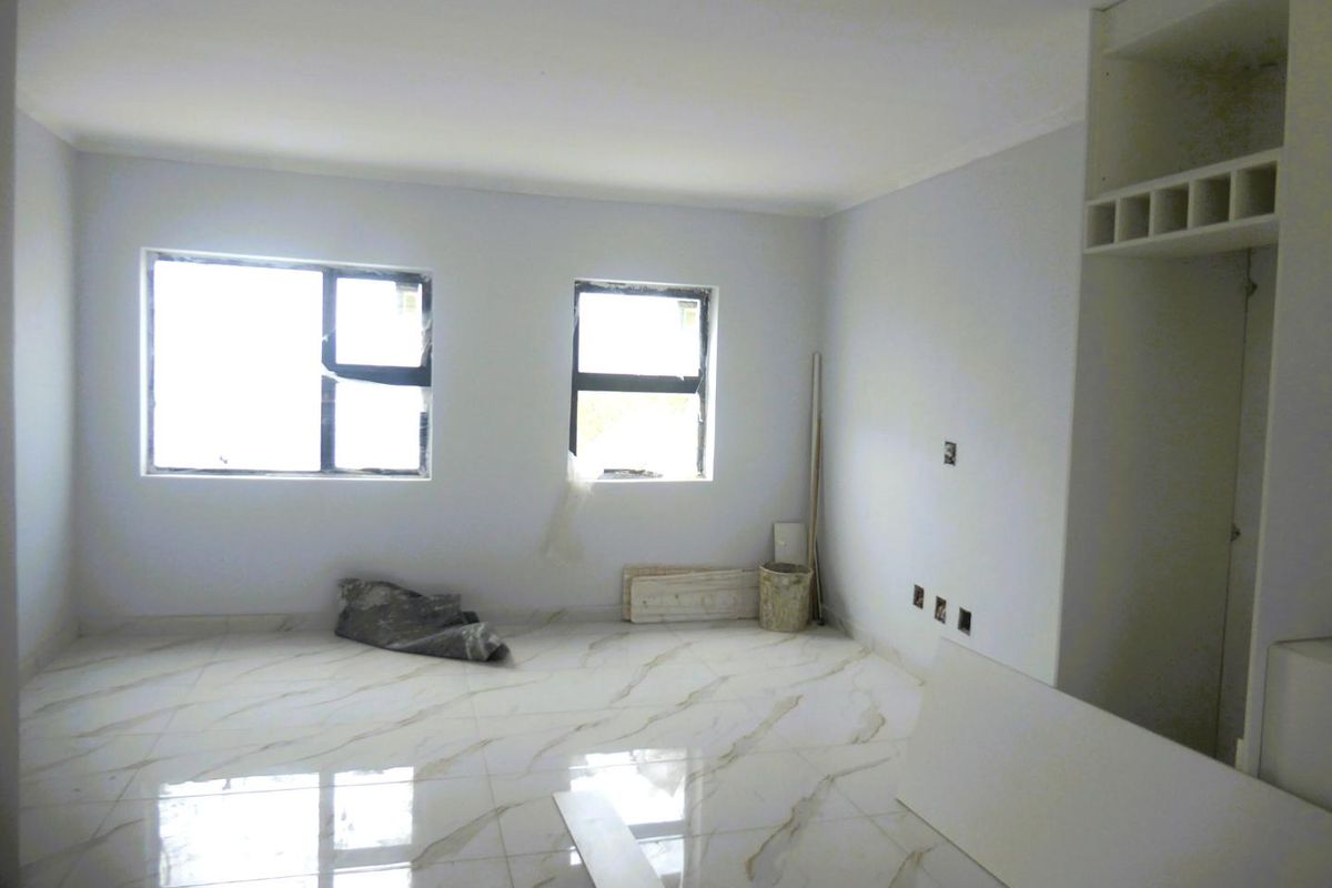 An empty living room featuring polished marble-look floor tiles, built-in shelving, and aluminium-framed windows, currently in a state of final construction finishing.