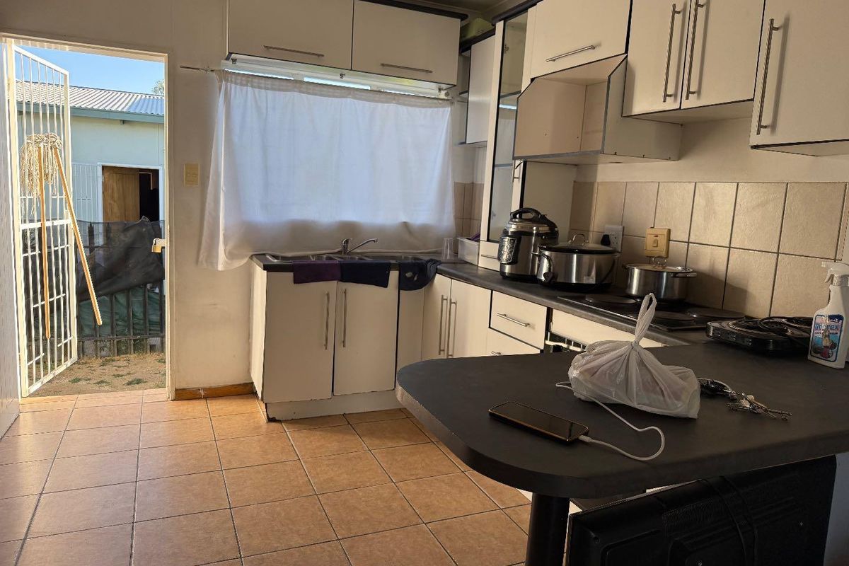 A functional kitchen featuring built-in cabinetry, laminate countertops, and tiled flooring, with direct access to the exterior through a security gate.