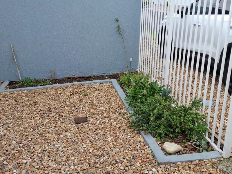 A small rear outdoor area featuring gravel ground cover, concrete garden borders, and white metal security fencing.