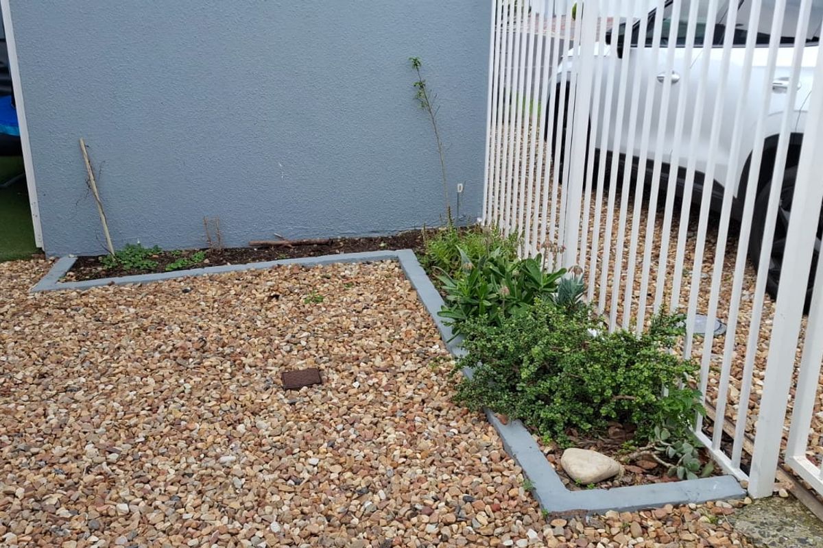 A small rear outdoor area featuring gravel ground cover, concrete garden borders, and white metal security fencing.