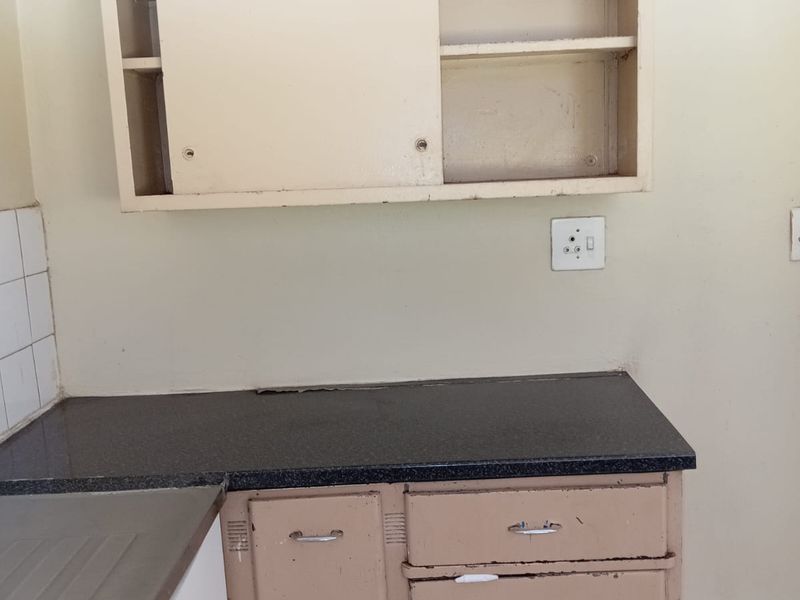A dated kitchen area featuring original built-in cabinetry, a dark laminate countertop, and a stainless steel sink, requiring cosmetic updates and refurbishment.