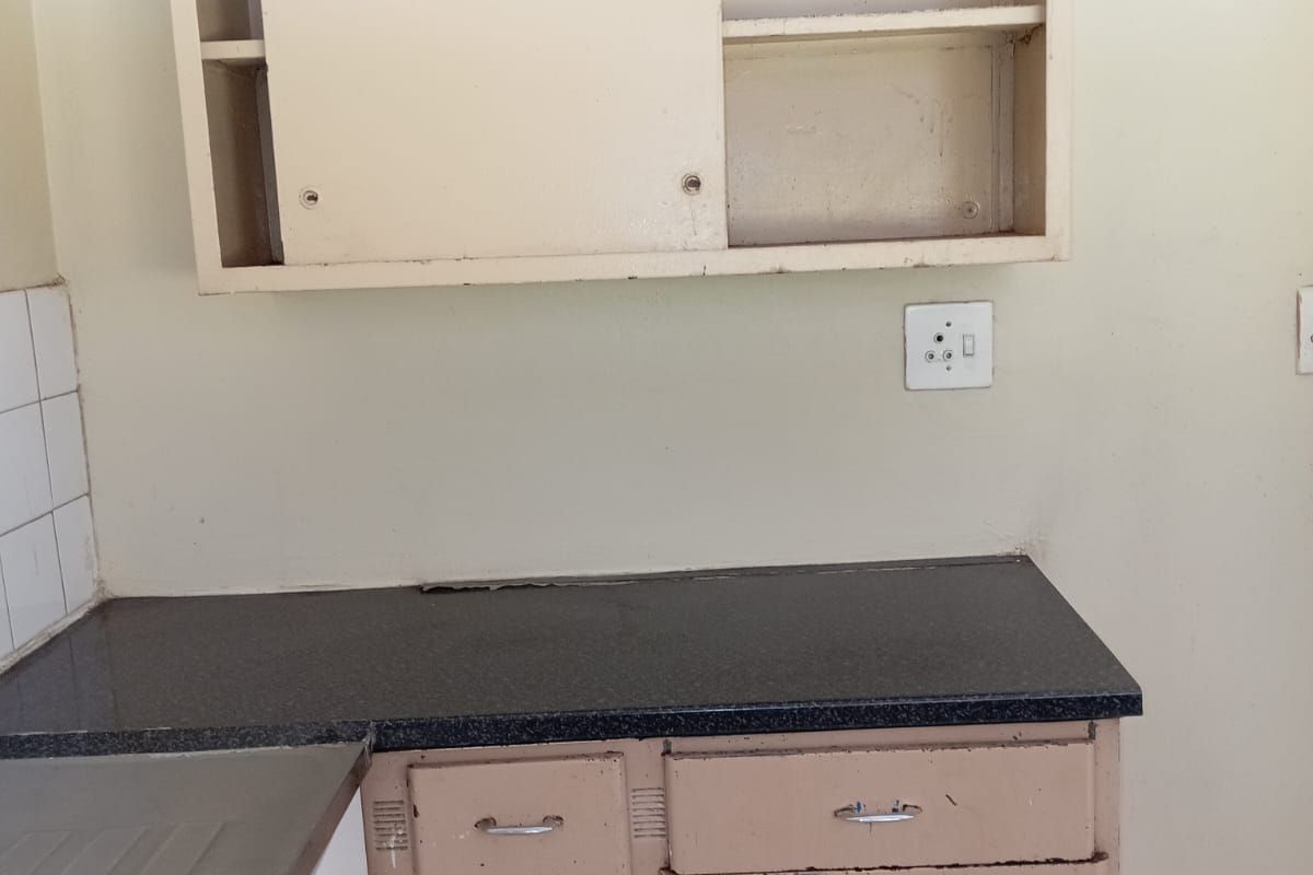 A dated kitchen area featuring original built-in cabinetry, a dark laminate countertop, and a stainless steel sink, requiring cosmetic updates and refurbishment.