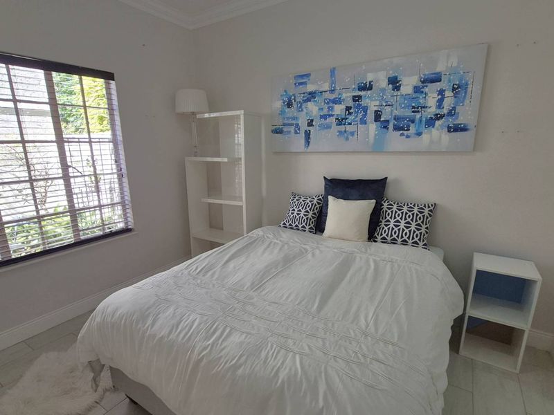 A bright bedroom featuring tiled flooring, crown molding, and large windows with fitted venetian blinds.