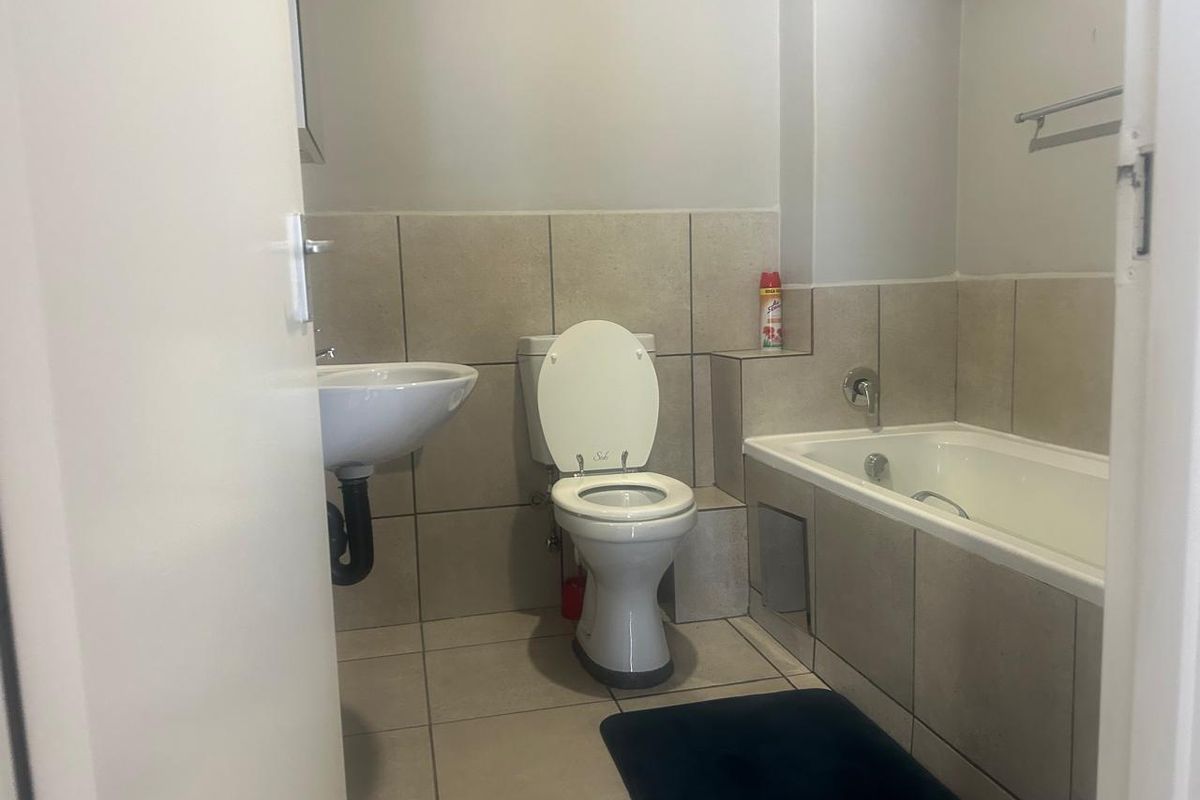 A functional bathroom featuring a standard bathtub, wall-mounted basin, and toilet with neutral floor and wall tiling.