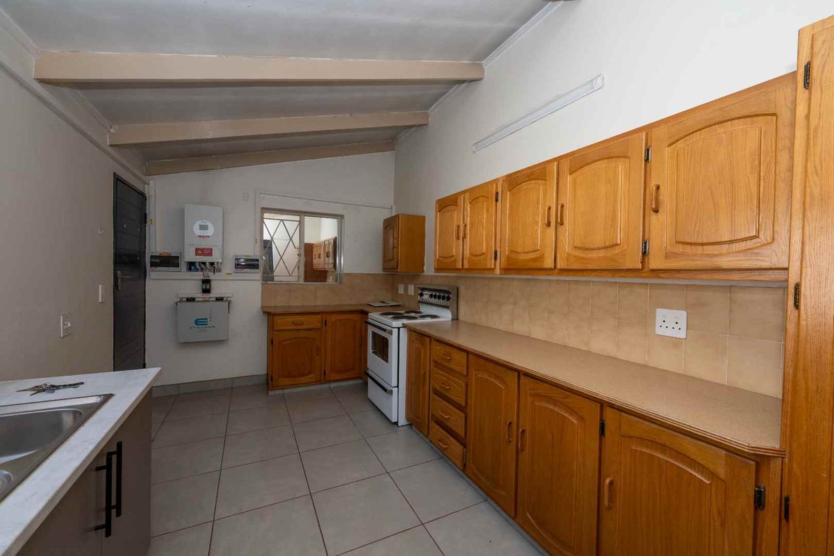 A functional kitchen featuring wooden cabinetry, laminate countertops, tiled flooring, and a freestanding stove, offering a practical layout with potential for modern updates.