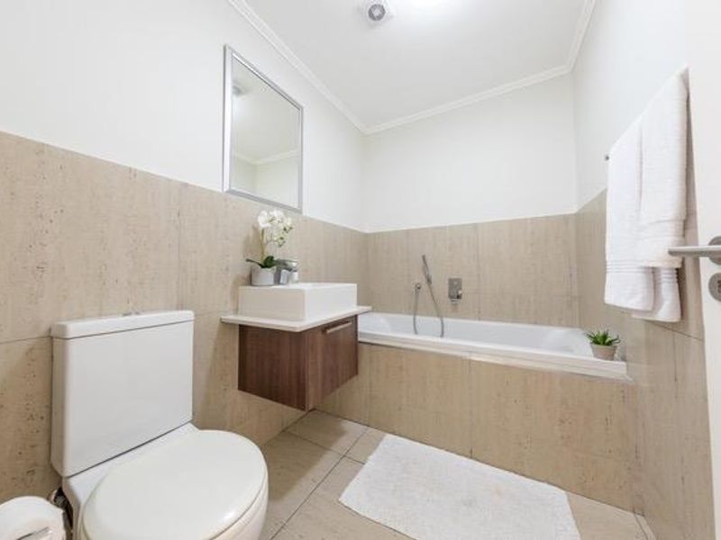 Modern bathroom featuring a wall-mounted vanity with vessel sink, built-in bathtub with handheld shower mixer, and neutral tiled finishes.