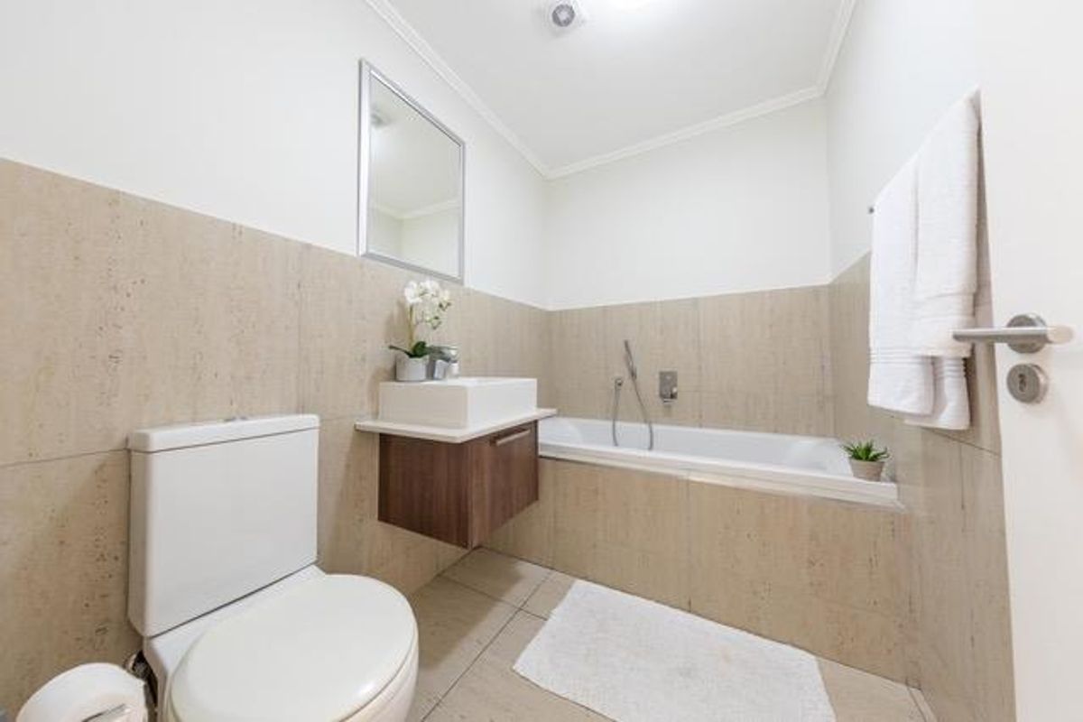 Modern bathroom featuring a wall-mounted vanity with vessel sink, built-in bathtub with handheld shower mixer, and neutral tiled finishes.