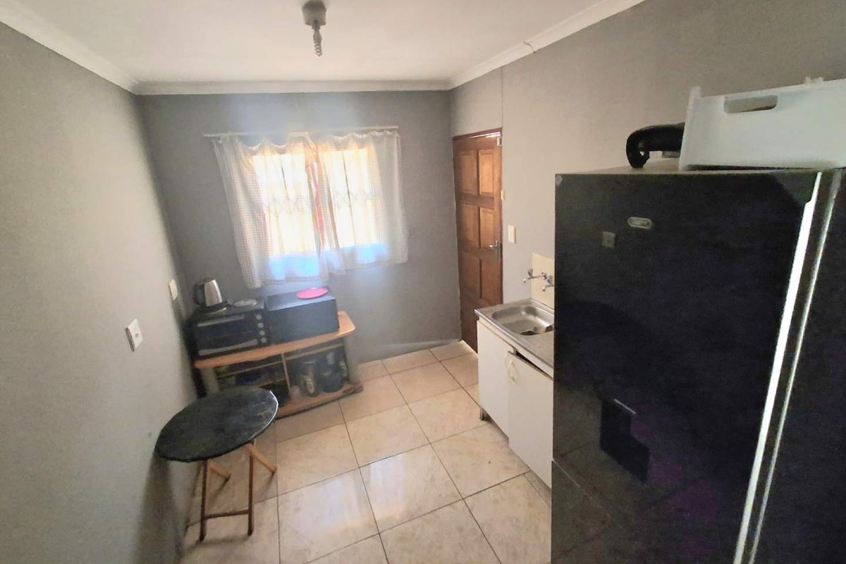 A compact kitchen area featuring tiled flooring, a single basin sink, and basic cabinetry. The space requires cosmetic updates to improve functionality and aesthetic appeal.