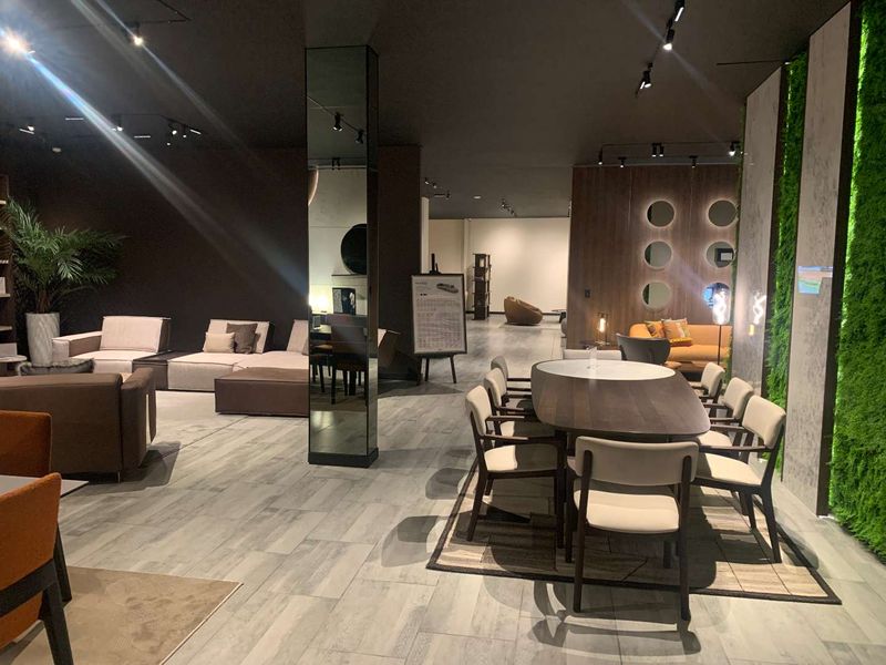 A modern, open-plan retail showroom space featuring contemporary track lighting, a mirrored structural column, and a decorative vertical garden wall.