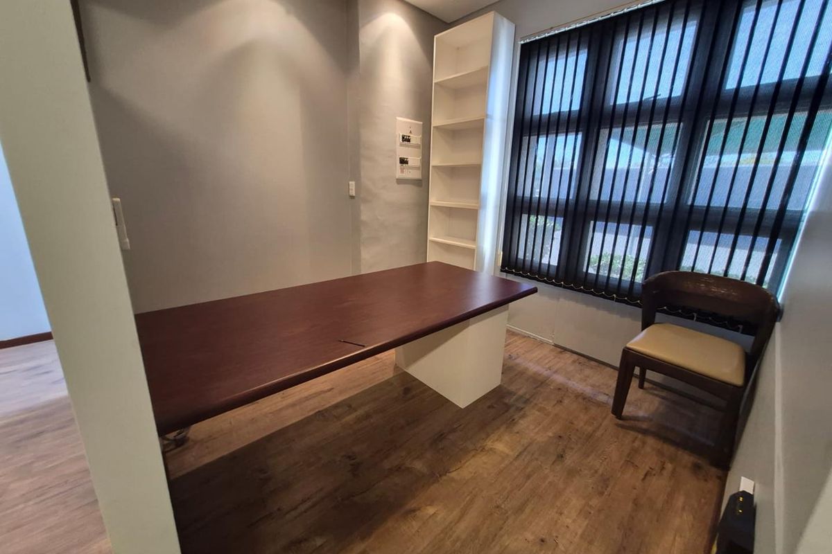 A functional office space featuring wood-look laminate flooring, built-in shelving, and large windows with vertical blinds, providing a professional work environment.