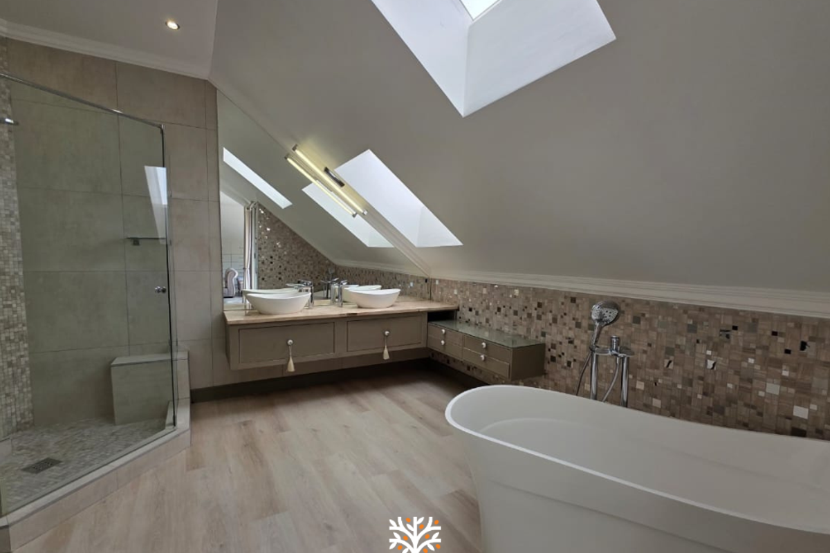 Modern attic bathroom featuring a glass shower enclosure, freestanding bathtub, dual vessel sinks on a wall-mounted vanity, and natural light from skylights.