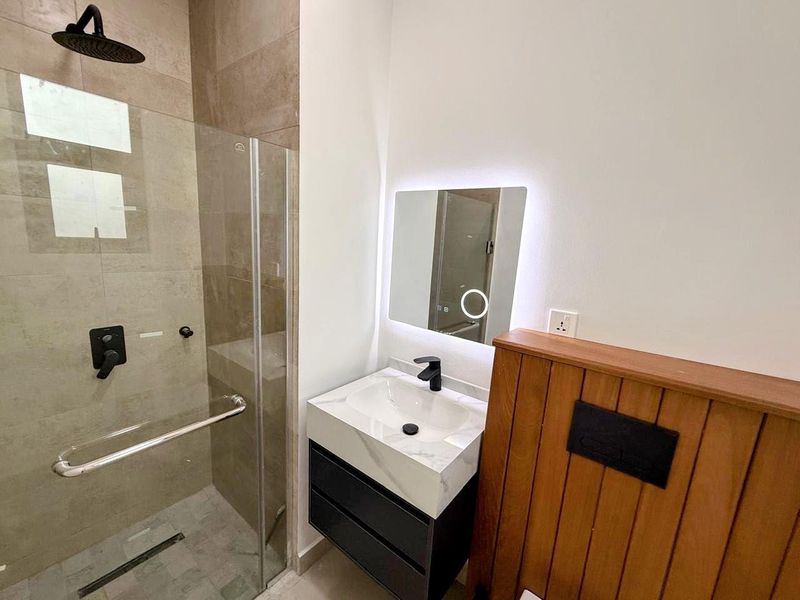 Modern bathroom featuring a glass-enclosed walk-in shower, contemporary vanity with marble-look countertop, and a sleek LED-backlit mirror.