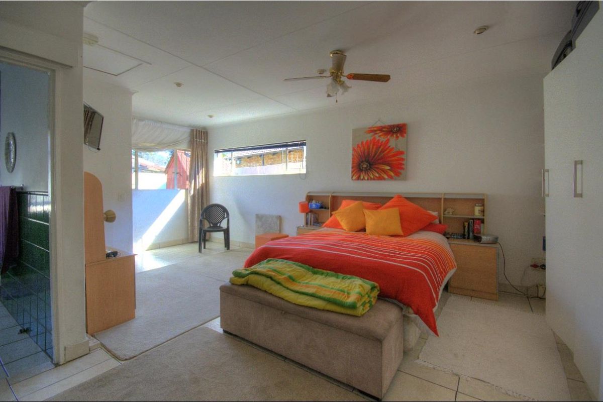 Spacious bedroom featuring tiled flooring, a ceiling fan, and a built-in headboard with access to an adjoining area.