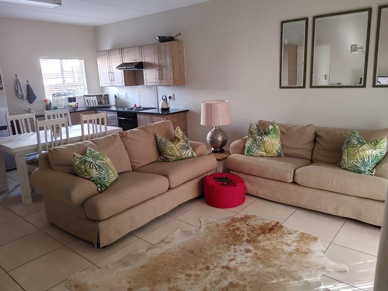 Open-plan living and kitchen area featuring tiled flooring, neutral cabinetry, and integrated kitchen appliances, creating a functional and connected living space.