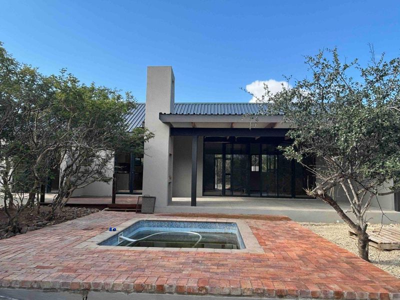 Rear exterior view featuring a brick-paved patio, a swimming pool, and a modern home with a corrugated metal roof and large sliding glass doors.