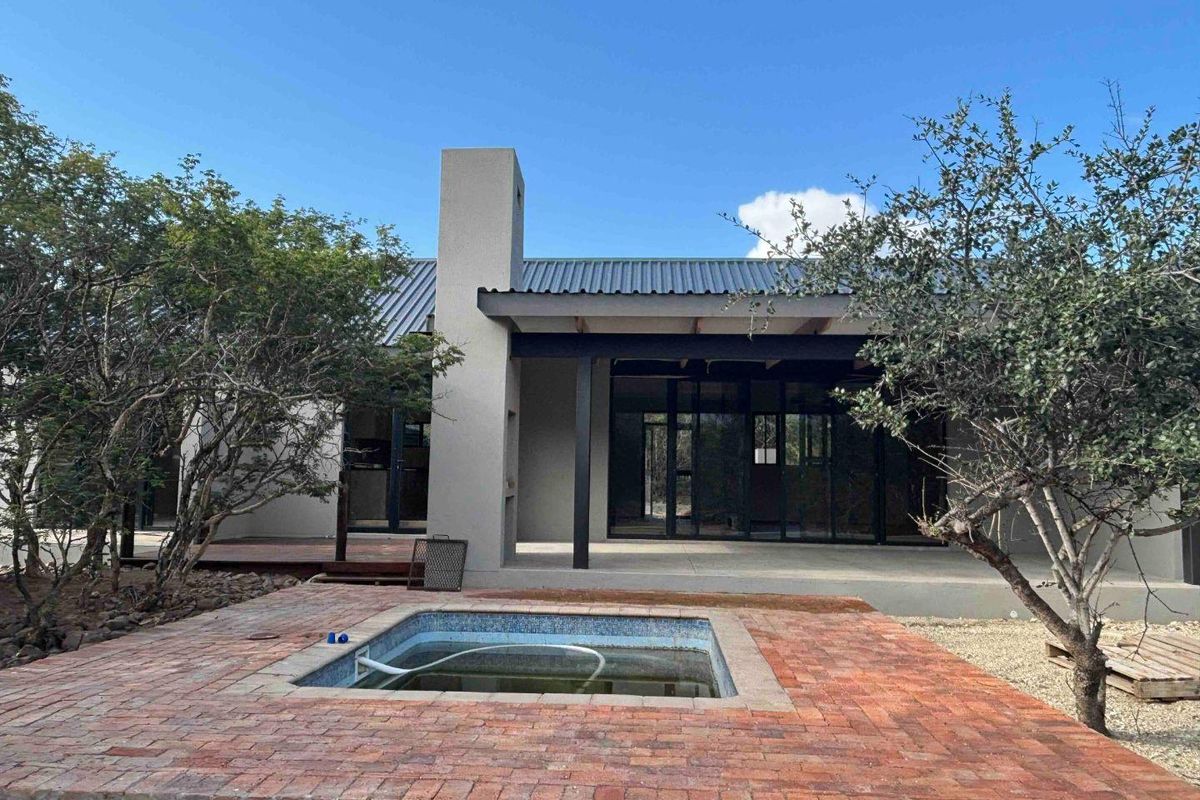 Rear exterior view featuring a brick-paved patio, a swimming pool, and a modern home with a corrugated metal roof and large sliding glass doors.