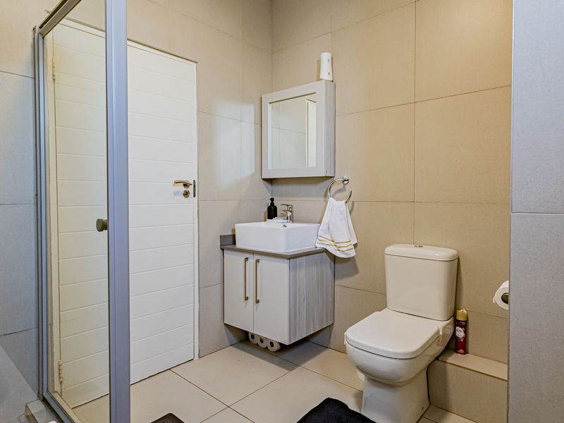 A modern bathroom featuring a glass shower enclosure, a contemporary vanity with a vessel sink, and neutral wall tiling.