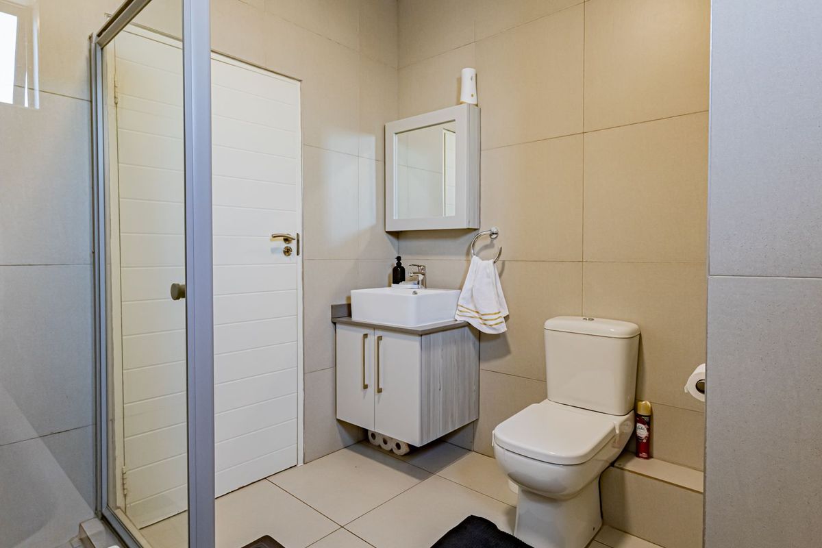 A modern bathroom featuring a glass shower enclosure, a contemporary vanity with a vessel sink, and neutral wall tiling.
