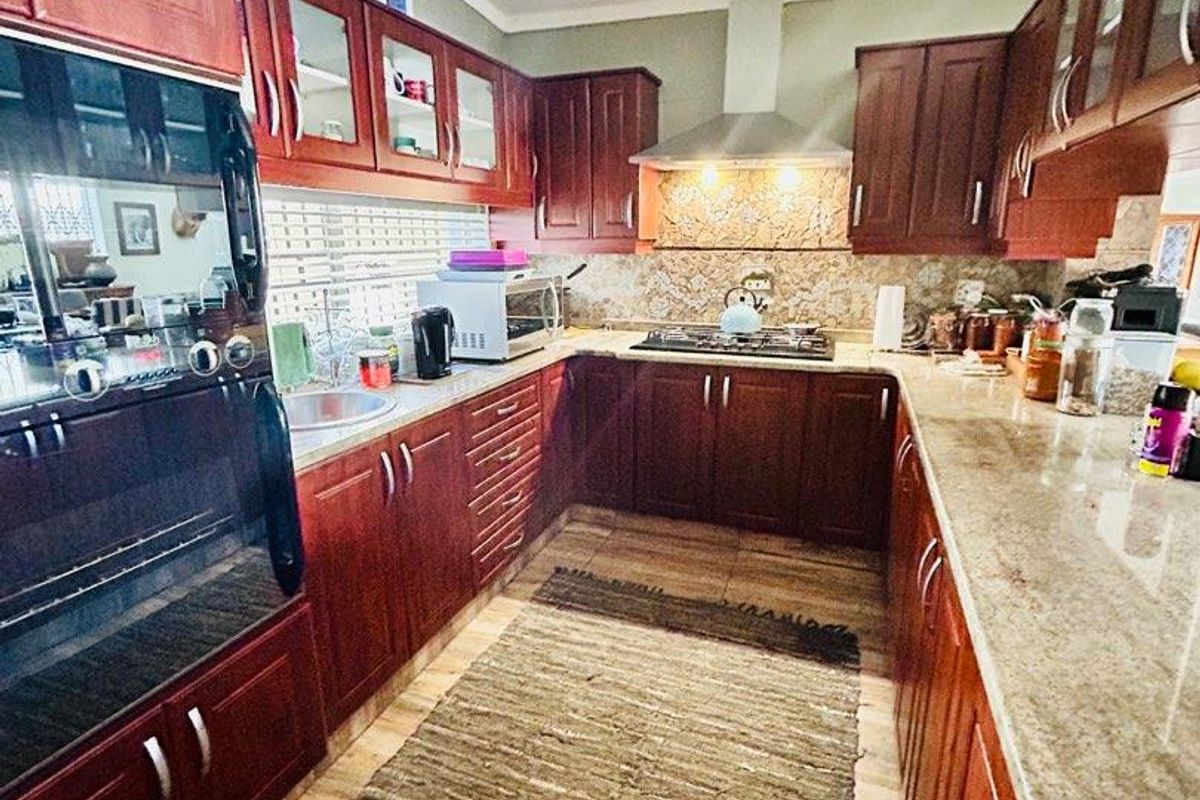 A functional kitchen featuring dark wood cabinetry, granite countertops, a built-in oven, and a stainless steel extractor fan.