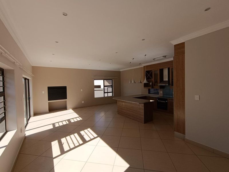 Spacious open-plan living and kitchen area featuring modern wood-finish cabinetry, a central island, tiled floors, and a built-in fireplace.
