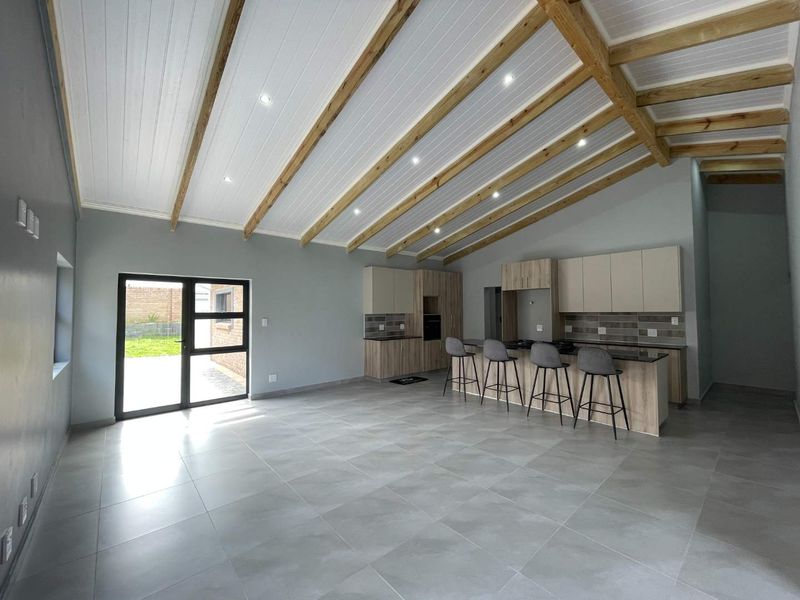 Modern open-plan living area featuring a contemporary kitchen with island, stone countertops, exposed timber ceiling beams, and large glass doors leading to the exterior.