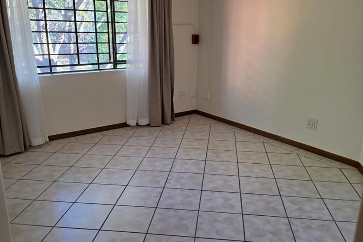 A bright, empty bedroom featuring tiled flooring, a ceiling fan, and a wall-mounted air conditioning unit, ready for personalization.