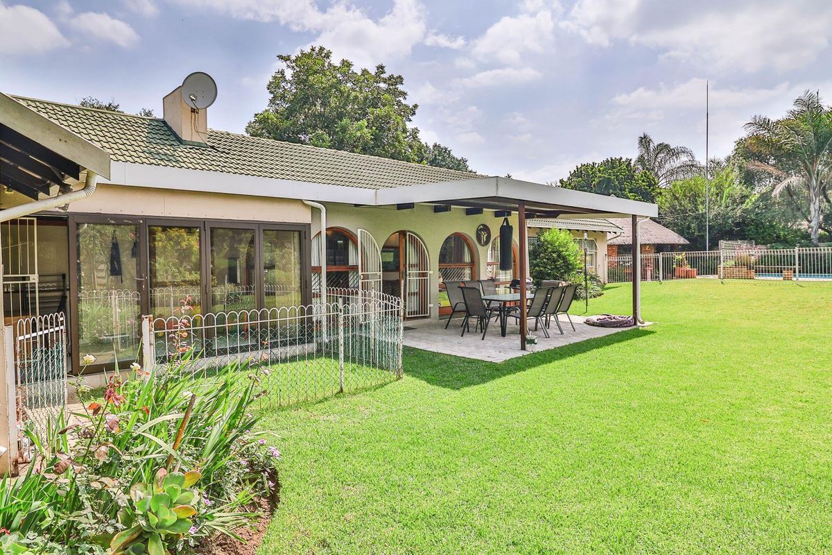 Rear view of the property featuring a covered patio area, tiled flooring, and a spacious landscaped garden with established lawn.