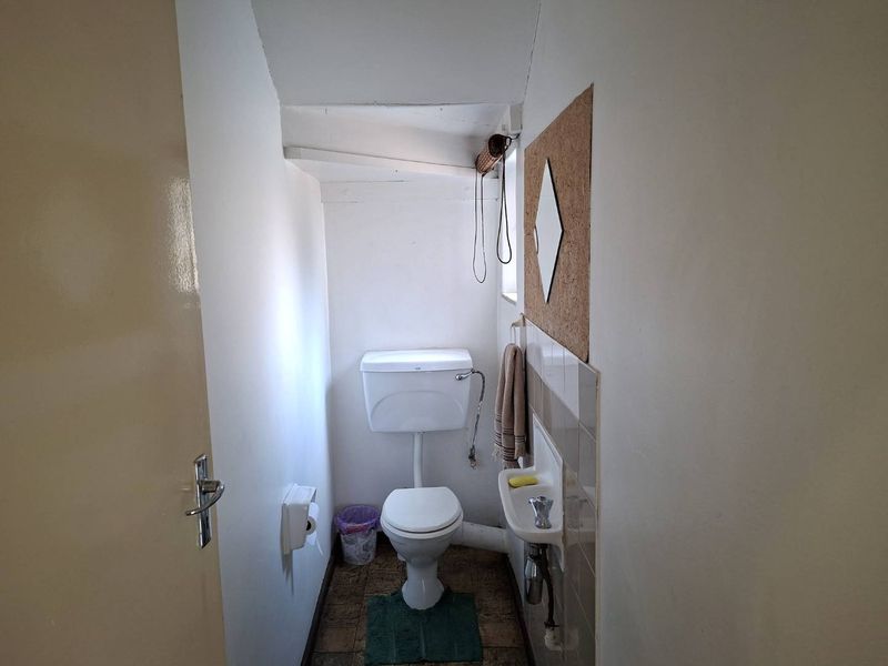 A compact guest bathroom featuring a standard toilet and a small wall-mounted basin with tiled splashback.