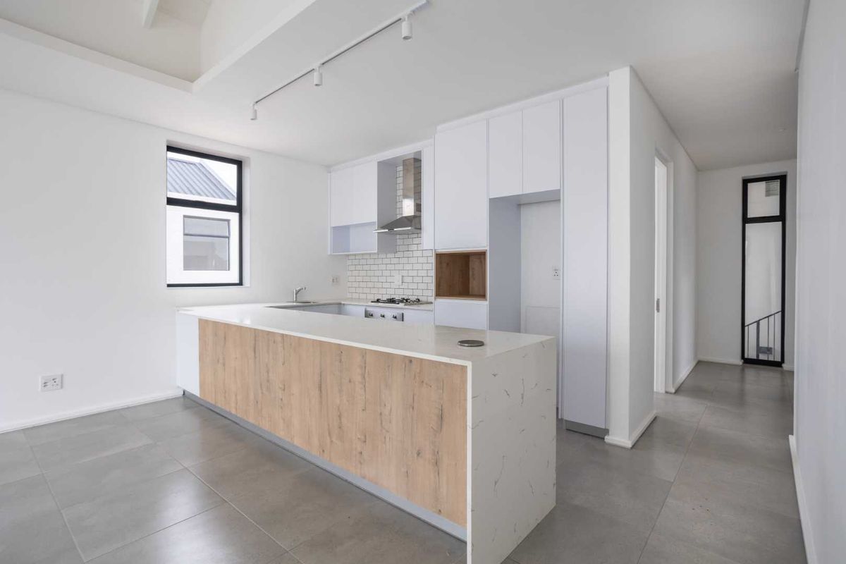 Modern kitchen featuring a large quartz-topped island, gas hob, stainless steel extractor, subway tile backsplash, and sleek white cabinetry with wood-grain accents.
