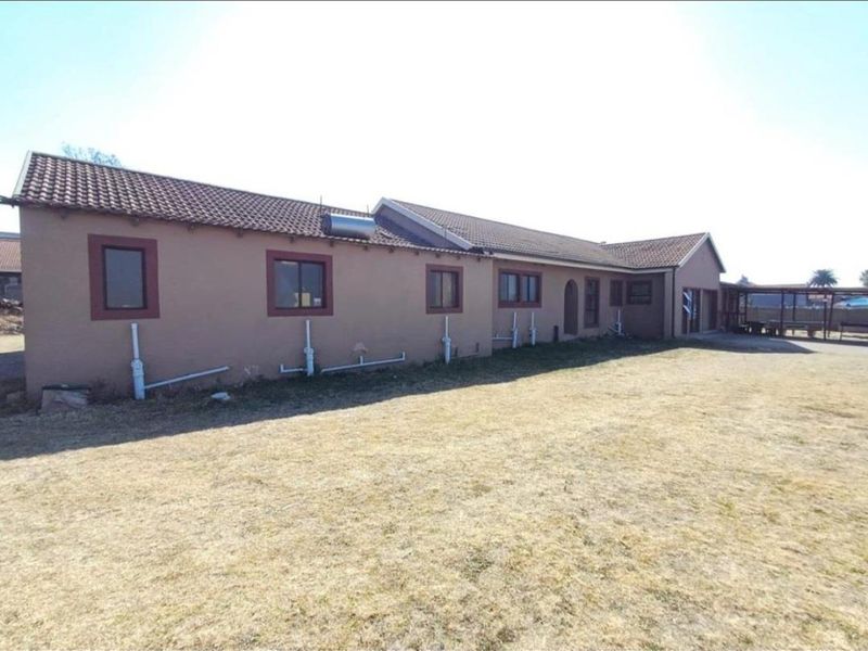 Rear view of the house featuring a tiled roof, solar water heater, and exposed exterior plumbing set against a large dry lawn area.