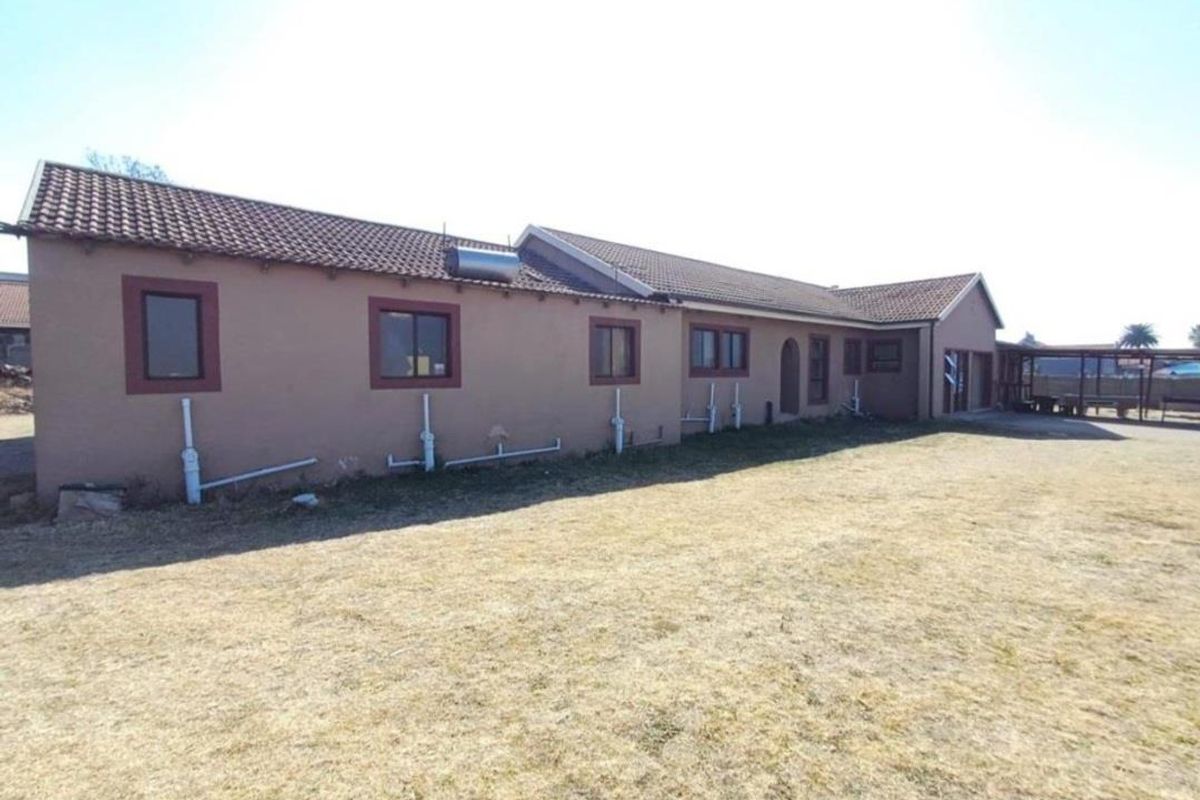 Rear view of the house featuring a tiled roof, solar water heater, and exposed exterior plumbing set against a large dry lawn area.